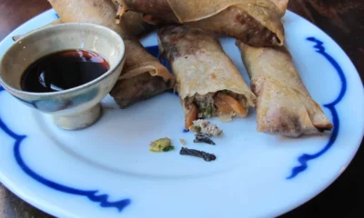 A plate of golden-brown shrimp-and-pork spring rolls, topped with fried shallots and paired with homemade chile sauce — a crispy, spicy, savory delight by Zang Toi.