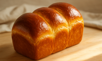 A golden loaf of extra-rich brioche, warm from the oven, its buttery layers glistening in soft morning light—proof that patience in baking always pays off.