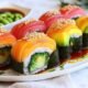 A fresh, hand-crafted rainbow roll glistens under the light — topped with vibrant sashimi and filled with crab, avocado, and cucumber.
