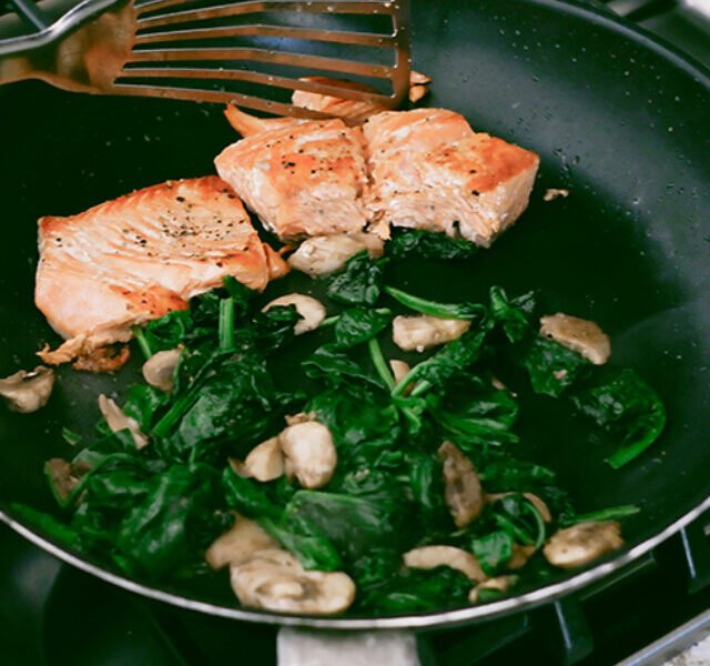 Woman Cooks Salmon With Spinach and Mushrooms